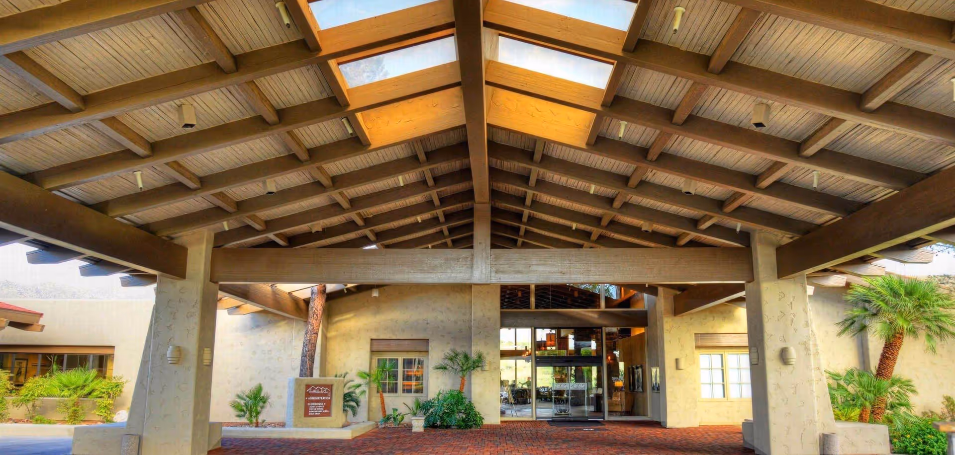 A canopy-covered building entrance with glass doors and palm trees at SaddleBrooke senior living.