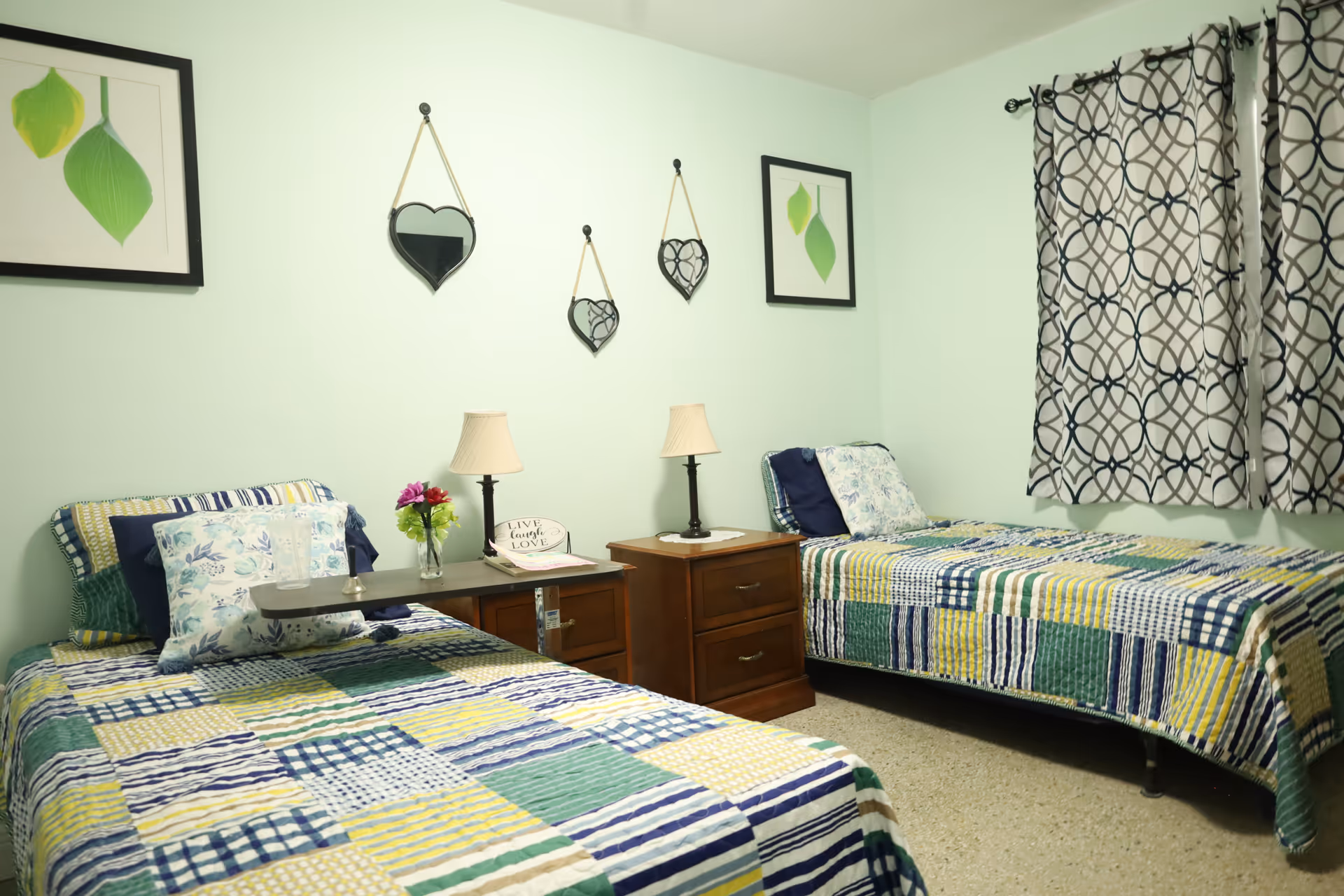Two twin beds with patchwork quilts, nightstands, lamps, and curtains in a shared bedroom.