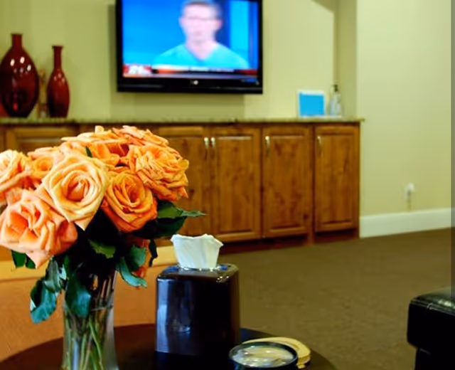 Bouquet of orange roses on a table in a lounge with a wall-mounted TV behind