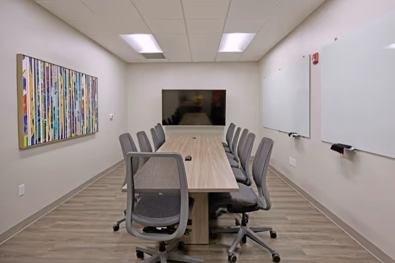 Conference room in a senior living facility with long table, chairs, whiteboards, and screen.