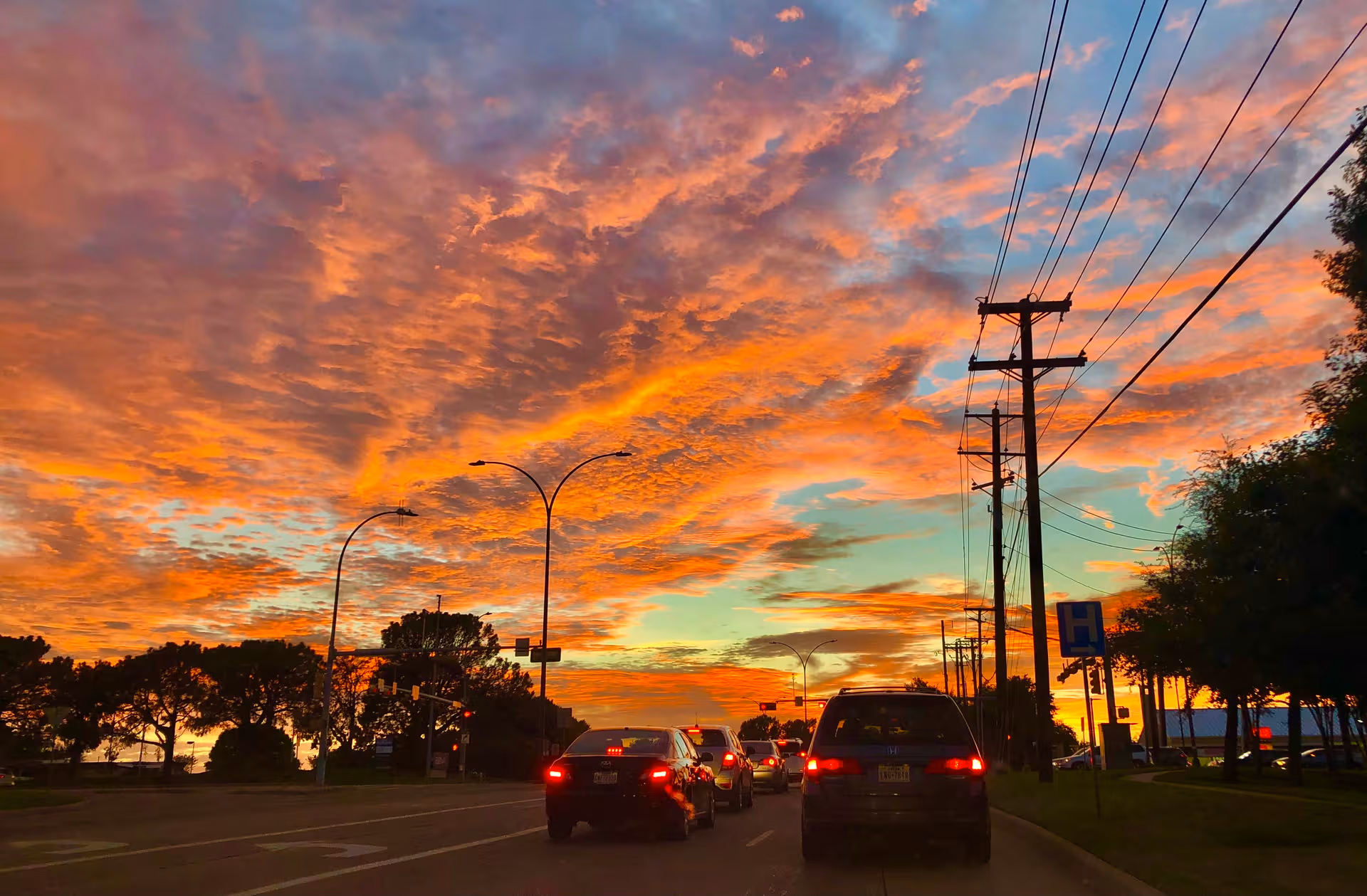 Sunset sky over a road with cars and power lines, trees along the curb.