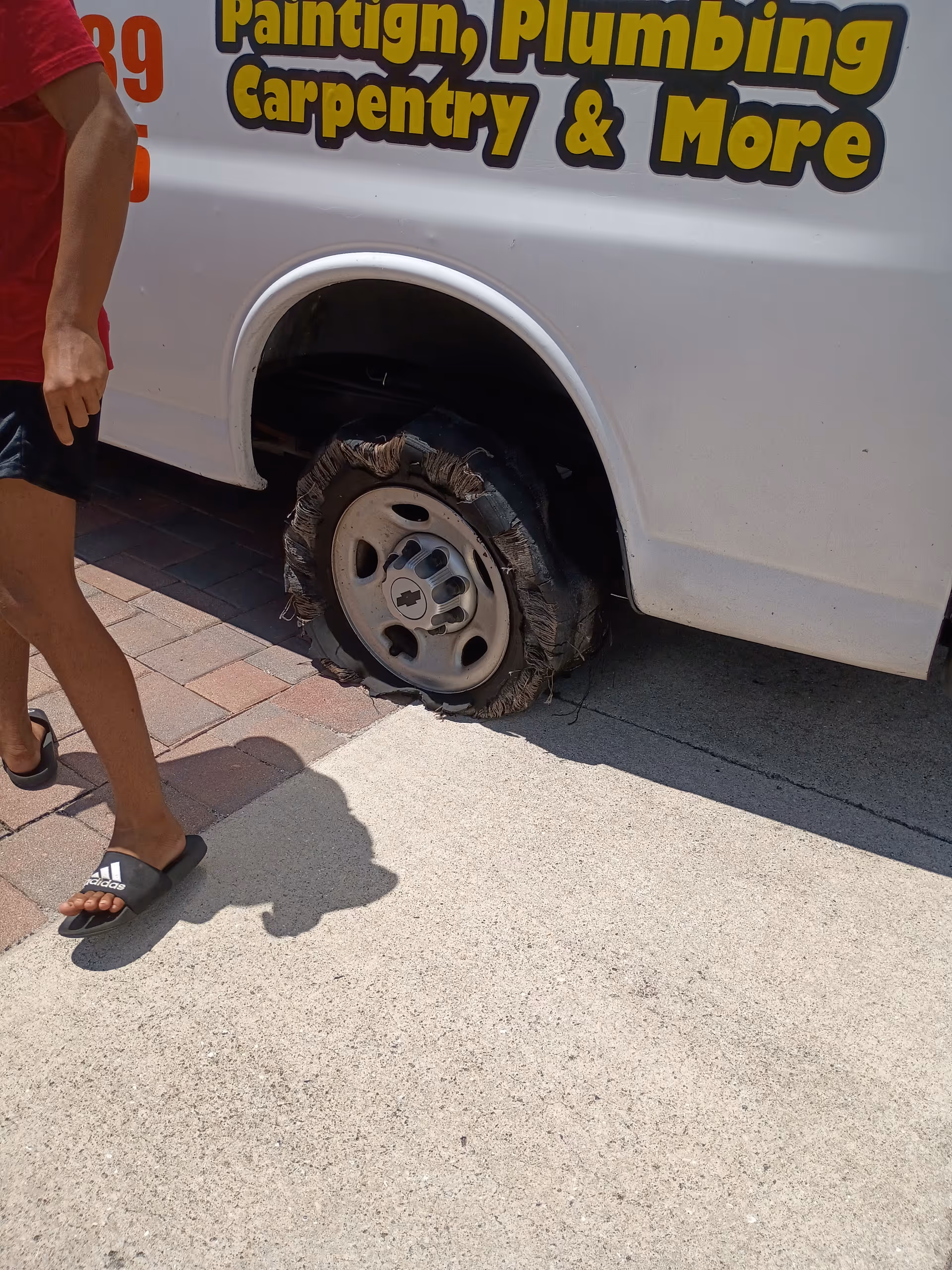 Partial view of a person beside a van with a flat tire outdoors.