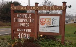 Outdoor wooden sign advertising Village Country Place, Richfield Chiropractic Center, and Older Wiser Life Services.