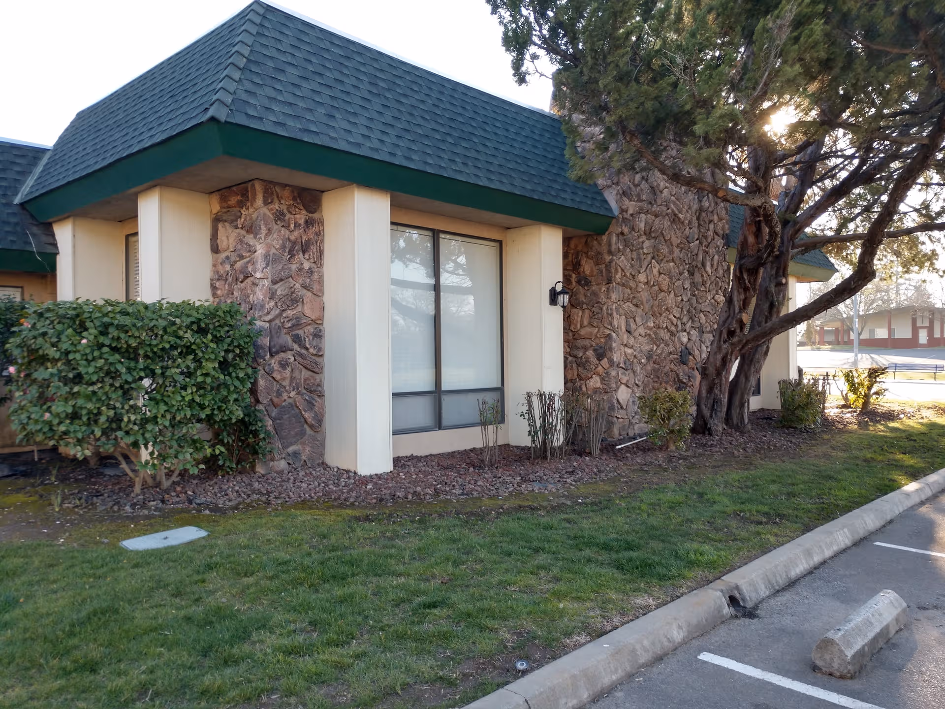 Exterior of Country Club Manor with stone walls, green roof, trees, and a parking lot.