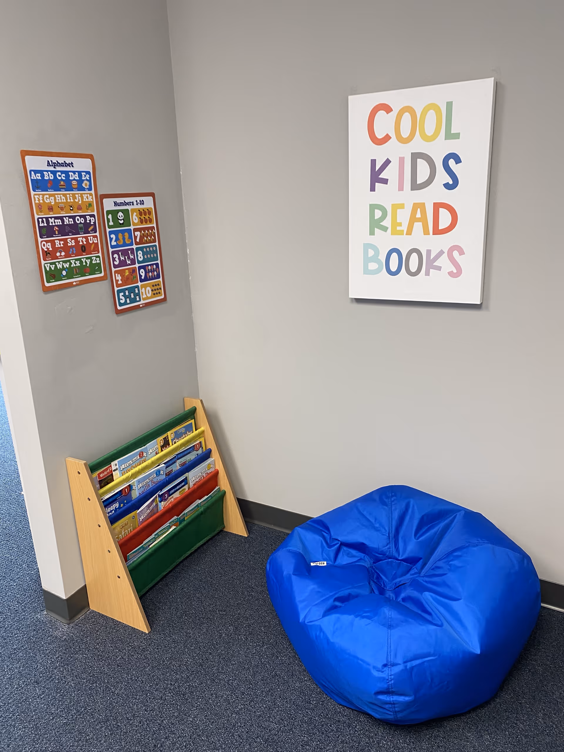 Corner reading nook with colorful posters, a small bookshelf, and a blue bean bag chair.