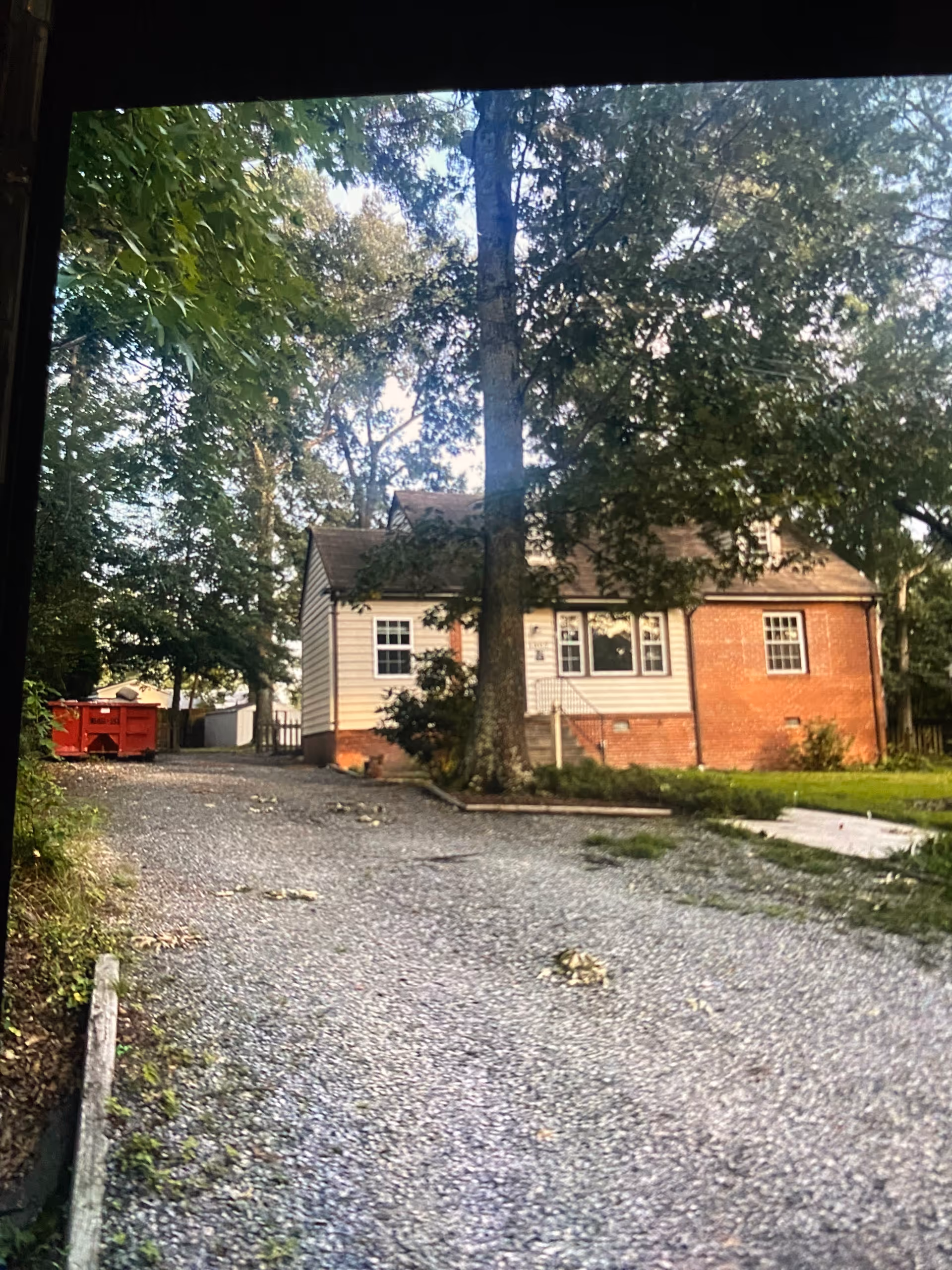 Front view of a brick and siding senior living facility with trees and gravel driveway.