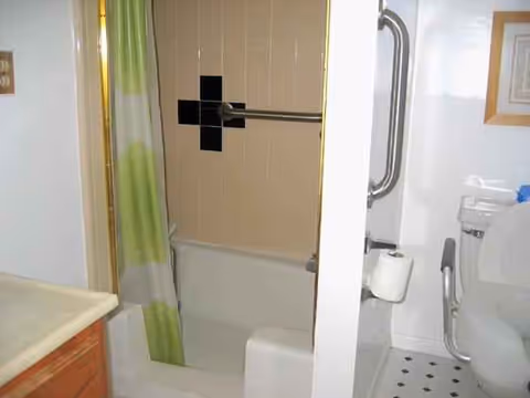 Accessible bathroom with bathtub, green curtain, and grab bars in Villa Mirage.