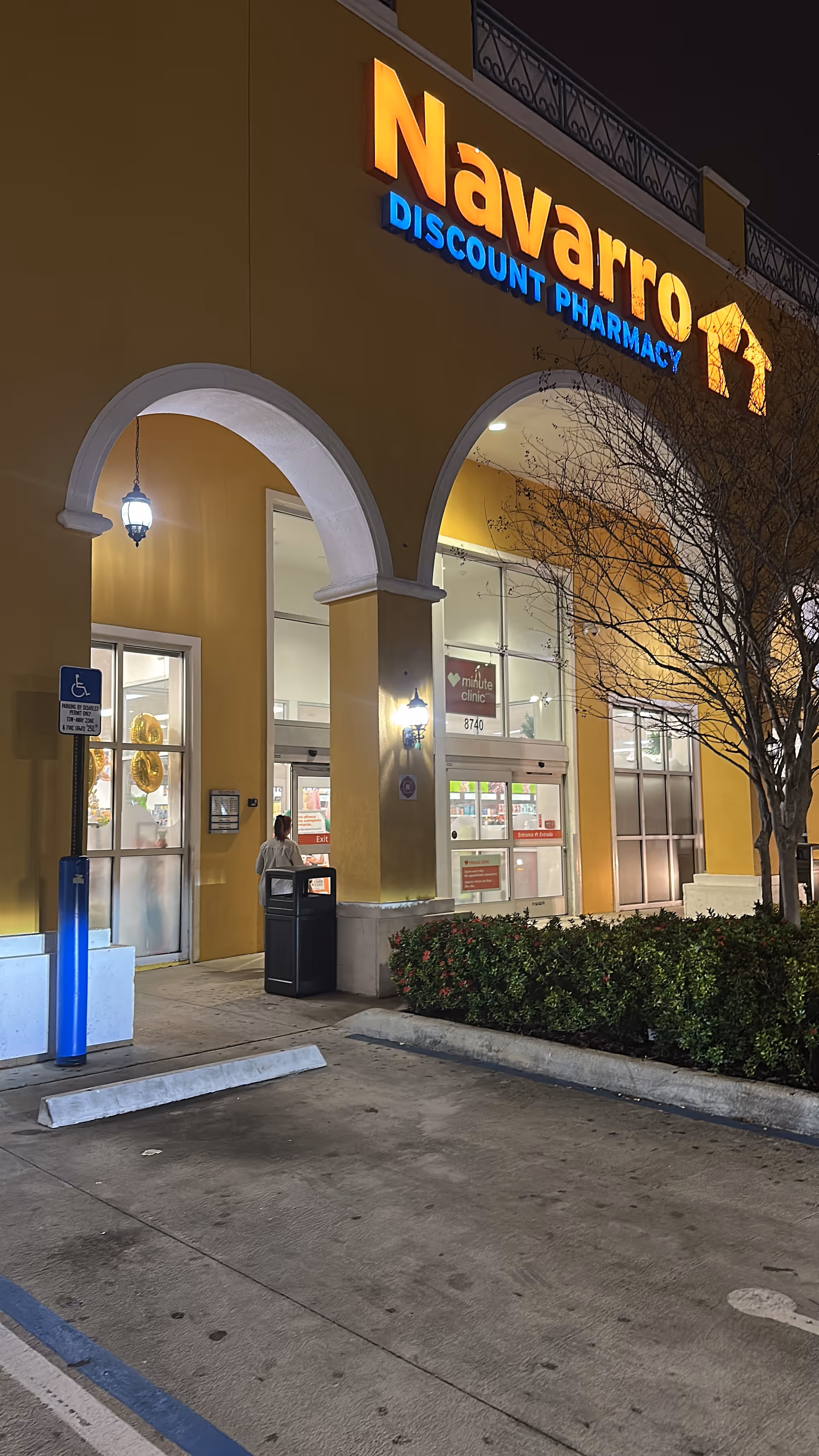 Navarro Discount Pharmacy storefront at night with arched entrance and a person near the door.
