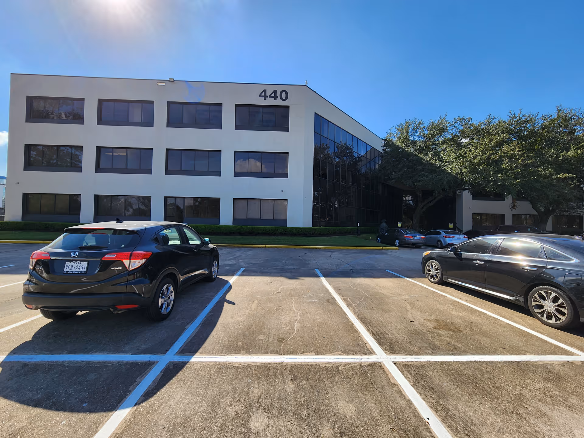 Modern white building with many windows and a glass-front facade, parking in front.