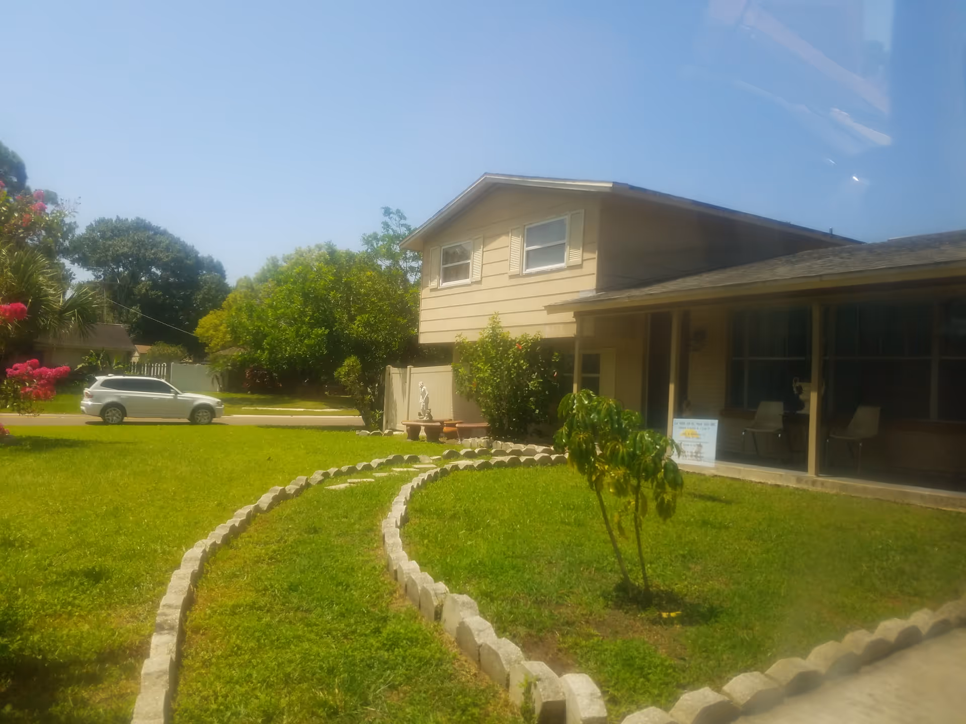 Exterior view of La Vida En El Mar: beige house, screened porch, curved stone borders, lawn.