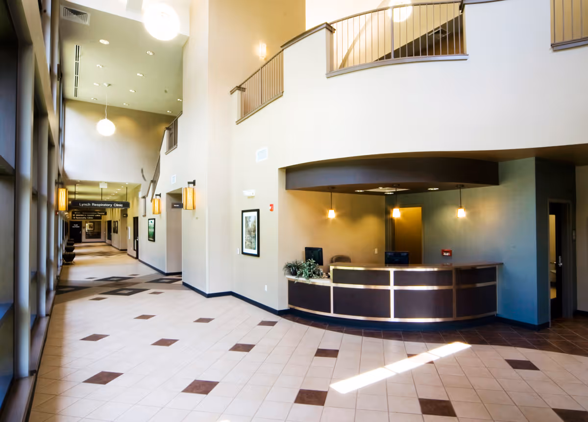 Spacious modern lobby with curved reception desk, long hallway, and upper-level balcony overlooking seating area.