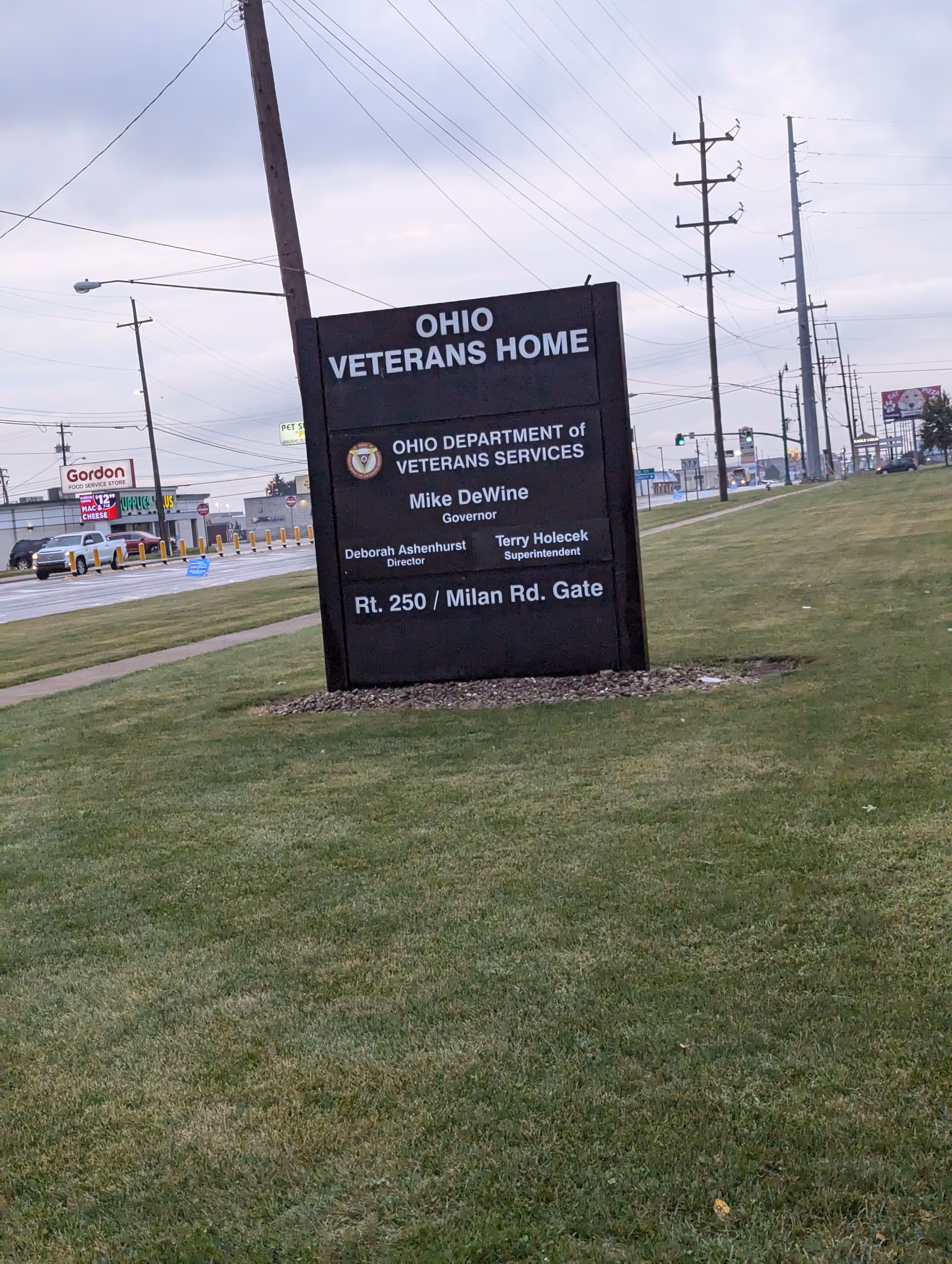 A large Ohio Veterans Home sign on a grassy roadside with power lines nearby