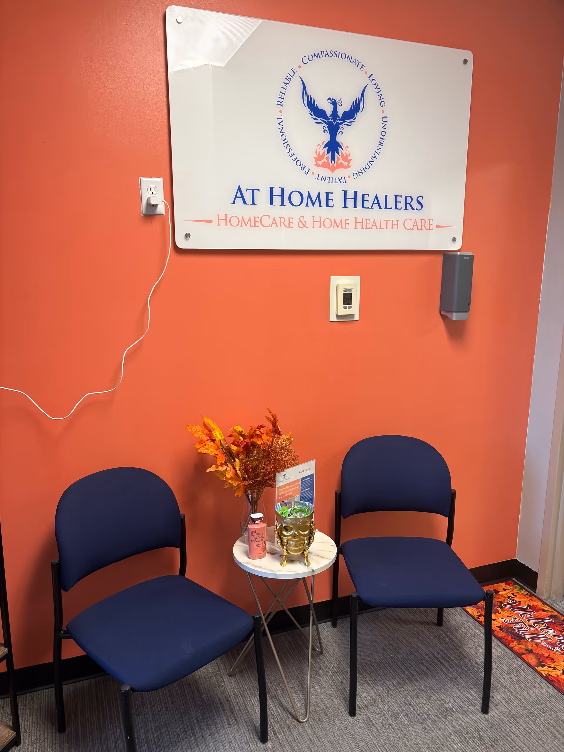 Two blue chairs flank a round table with decor against an orange wall featuring a sign.