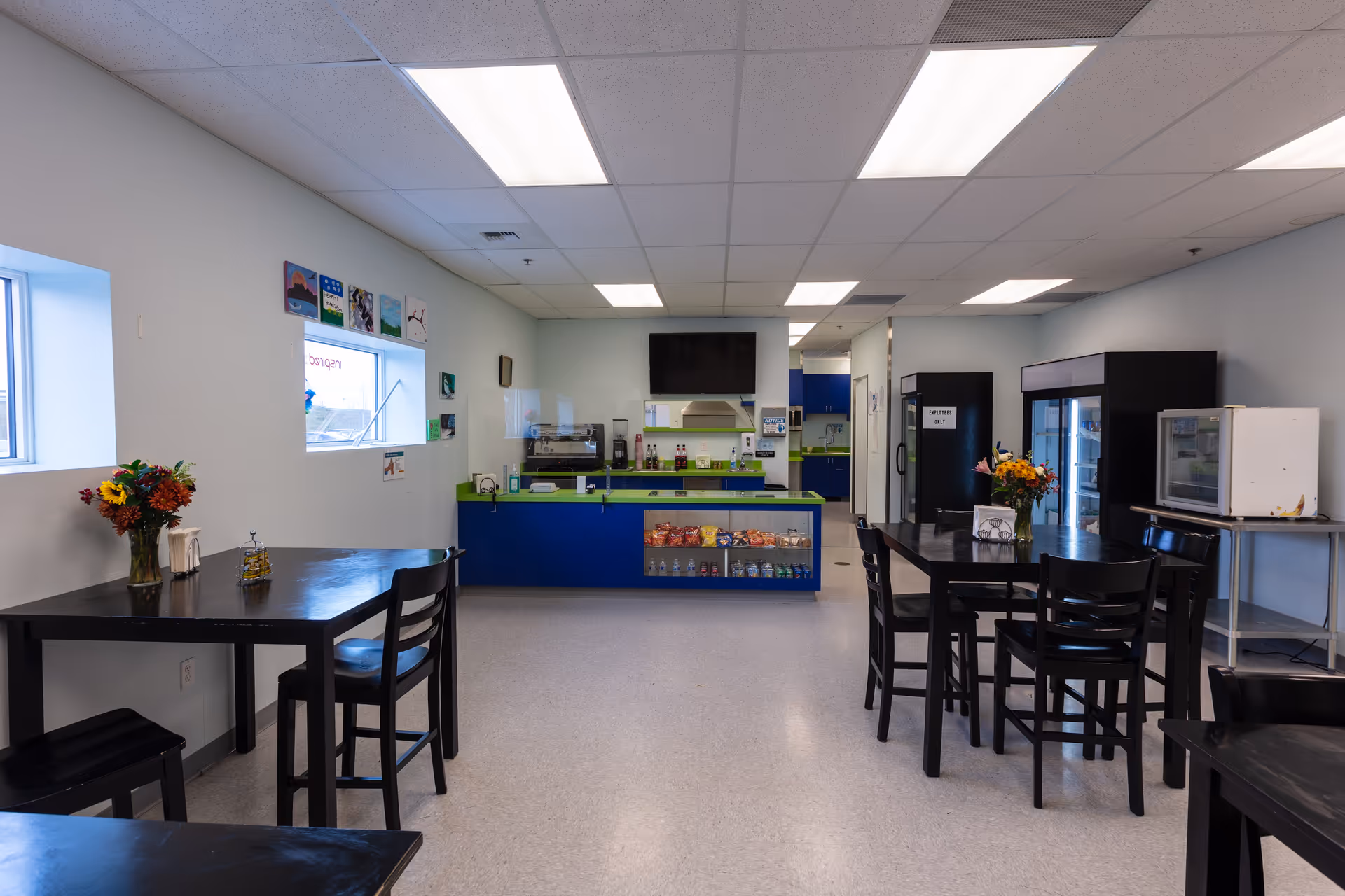 Bright dining area with black tables, chairs, a serving counter, and snack display.