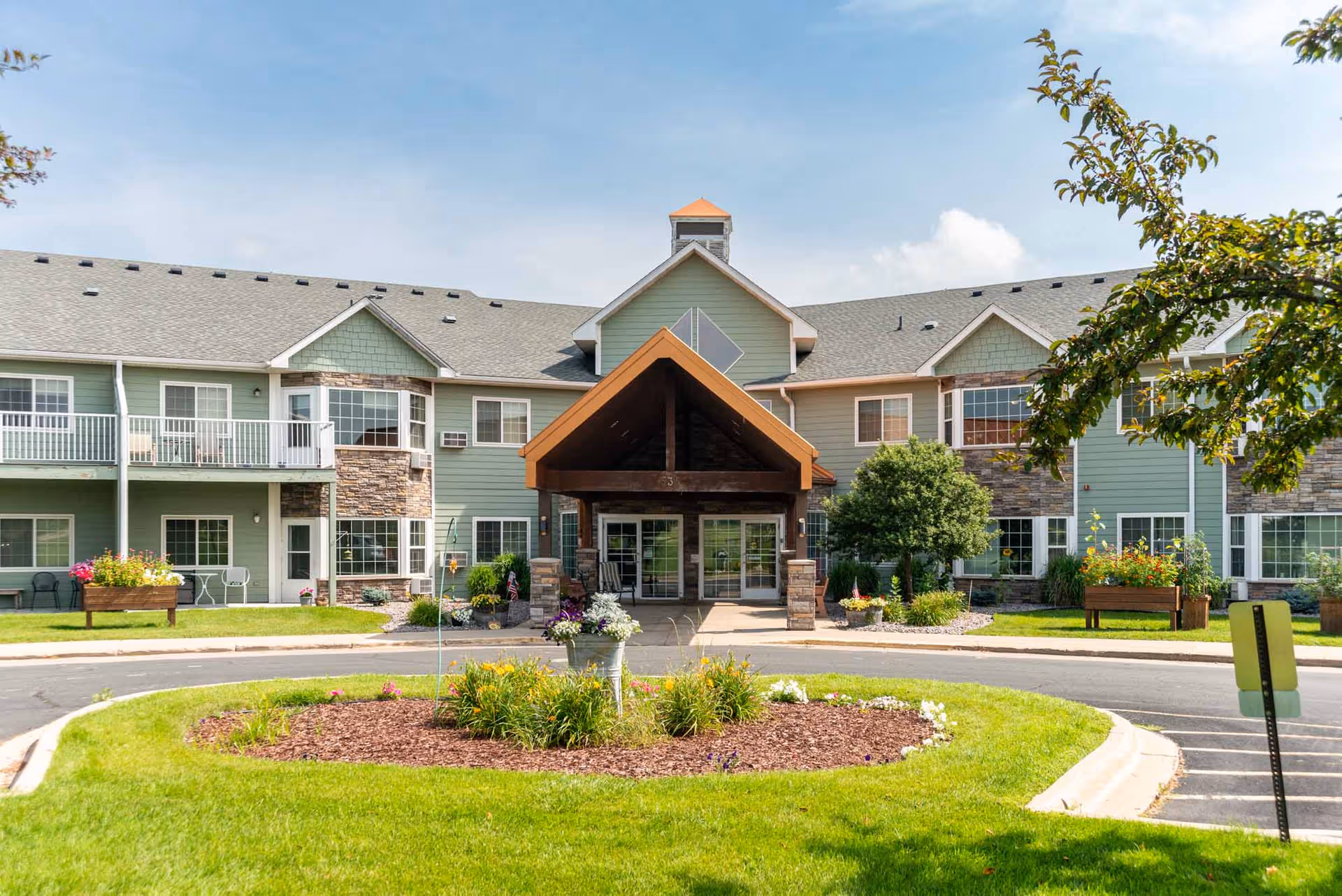 Front exterior of Arbor Garden Place senior living facility with green siding and landscaped entrance.