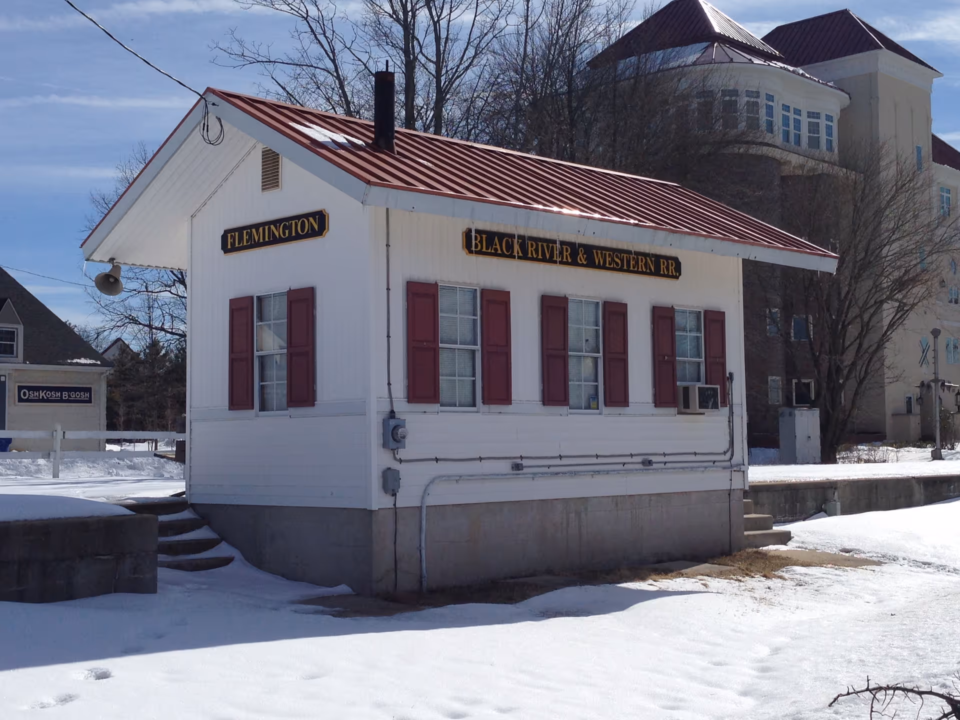 Small white train station with red roof and shutters beside snow.