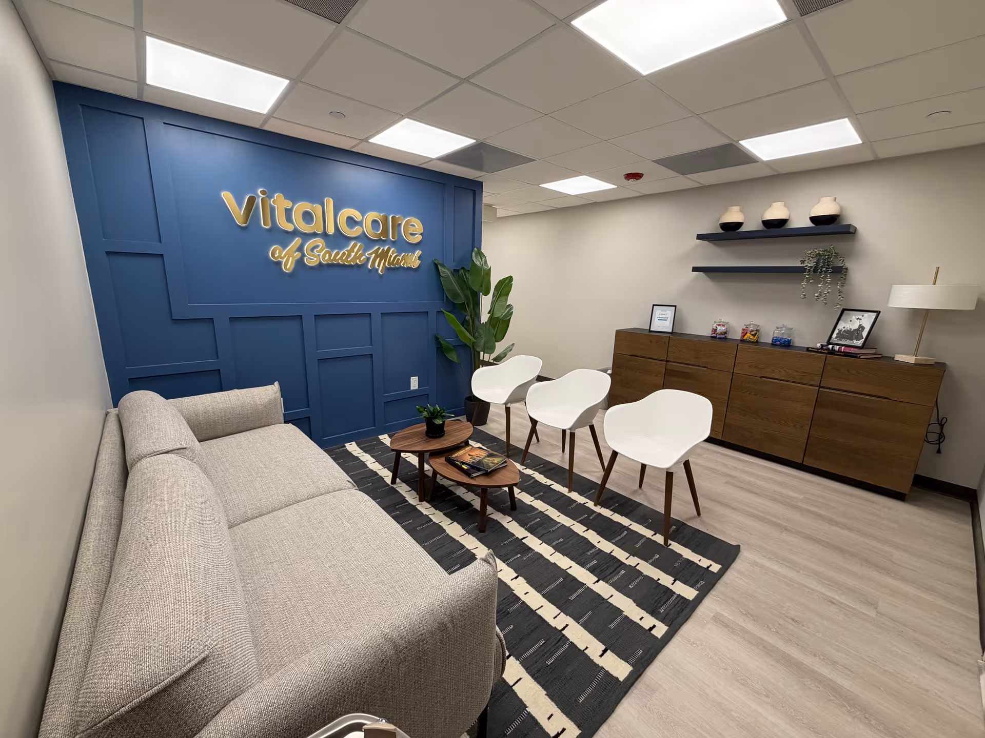 Lobby area featuring a blue panel wall with 'Vitalcare of South Miami' and comfortable seating.