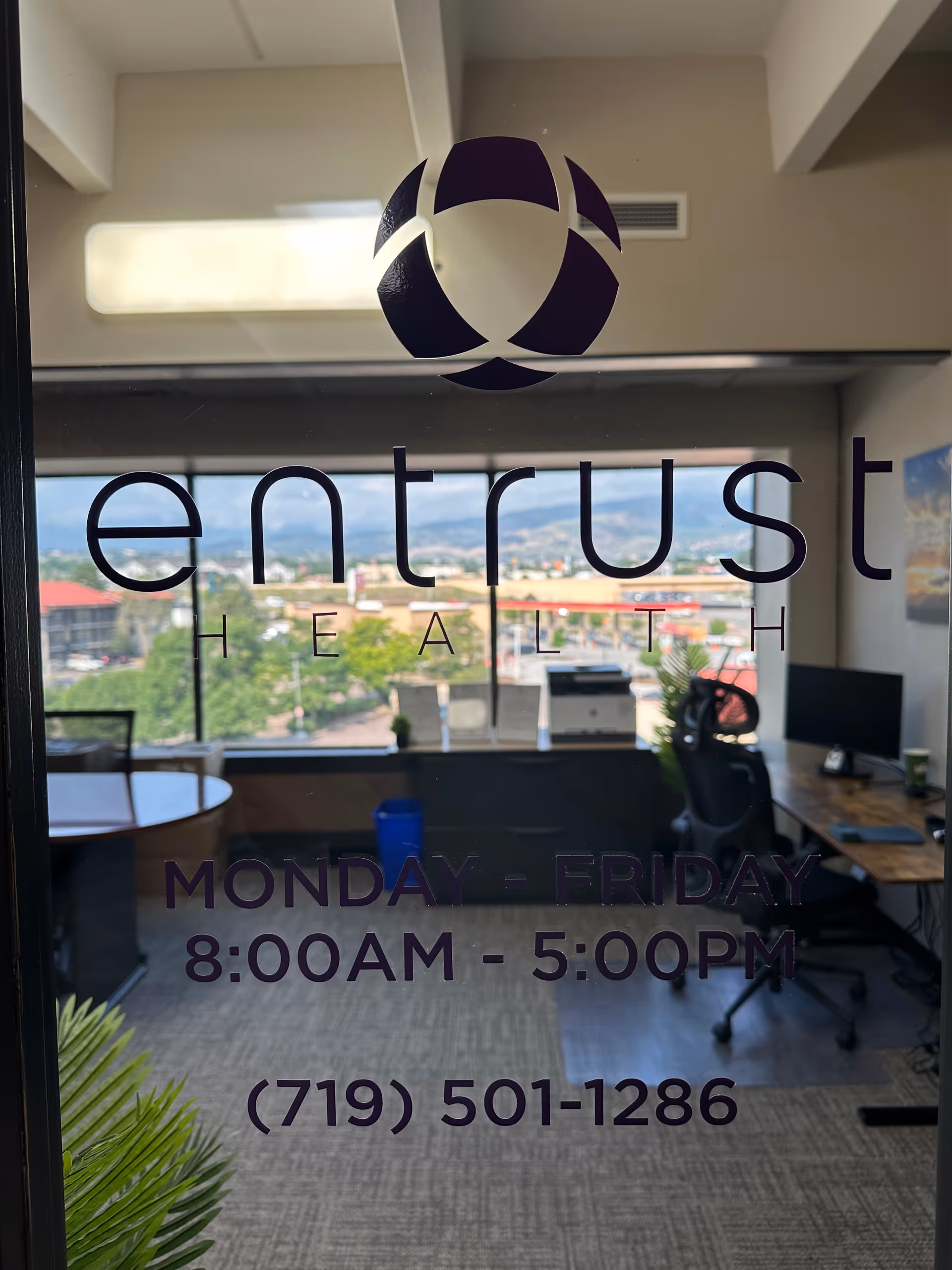 Office interior visible through glass door featuring Entrust Health logo and hours.