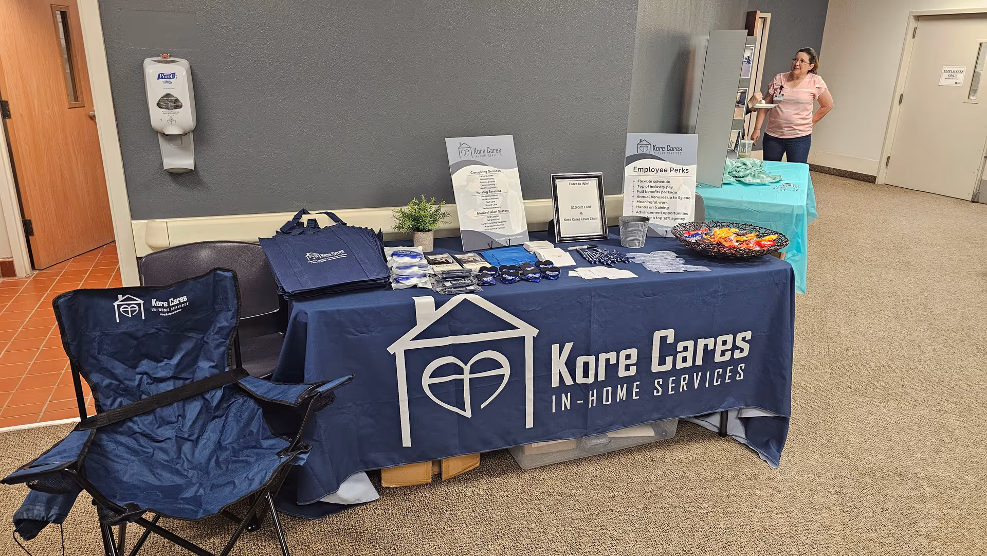 Promotional table with Kore Cares banner and giveaway materials inside a facility lobby.