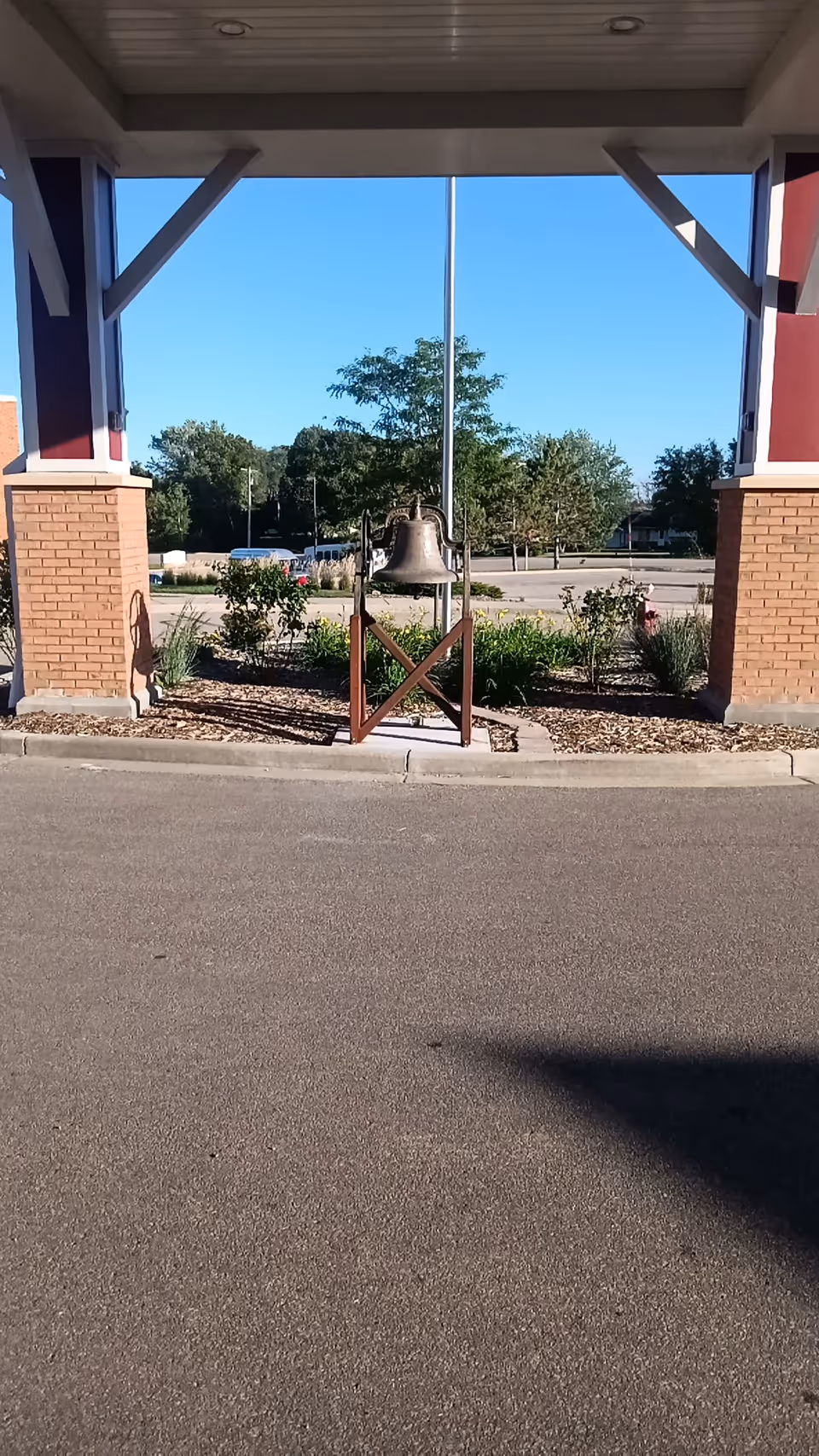 Covered entrance of Kitty Rhoades Memorial Memory Care Center with a bell and landscaping.