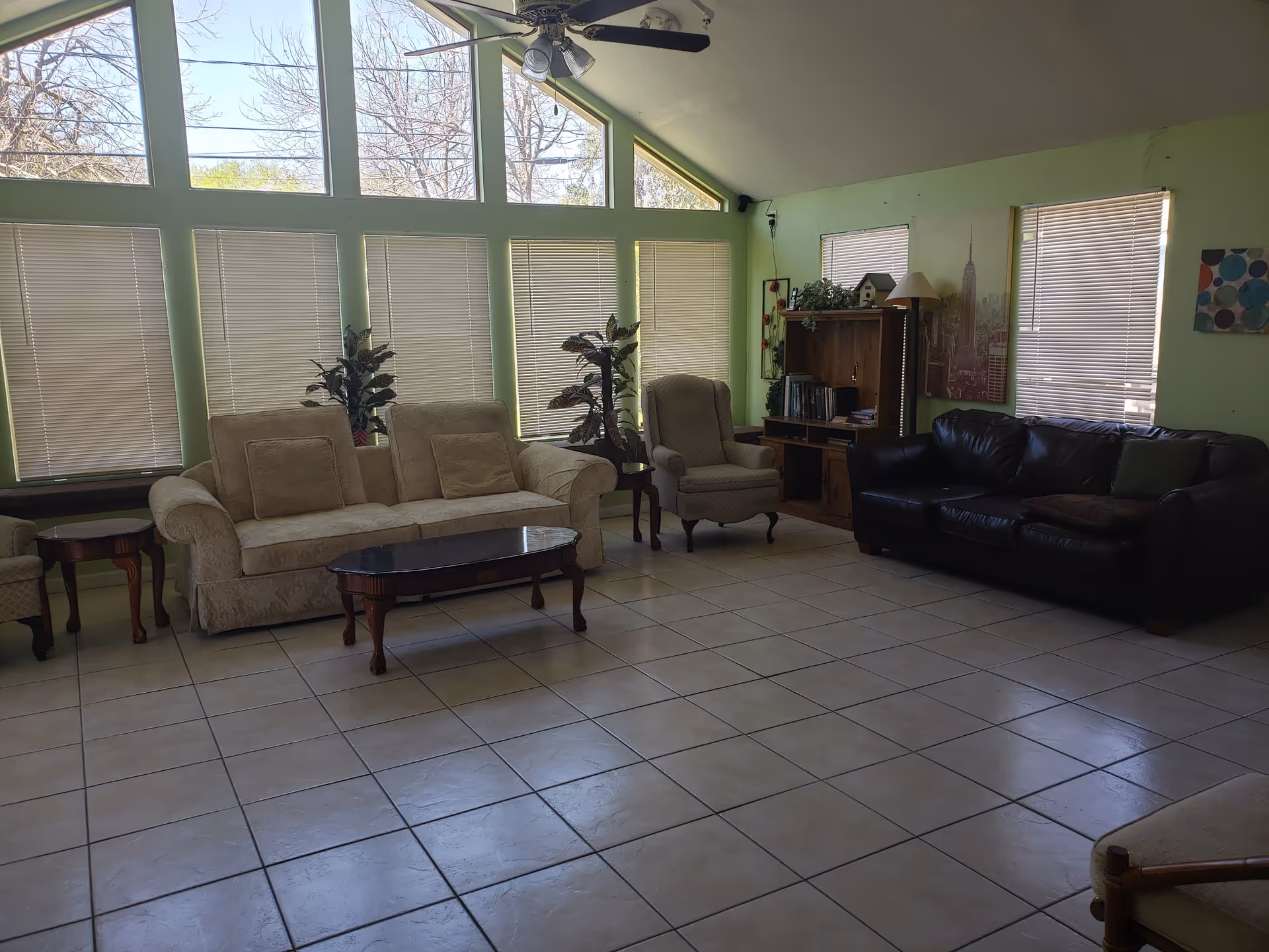 Lounge area with beige and black sofas, chairs, and large windows with blinds.