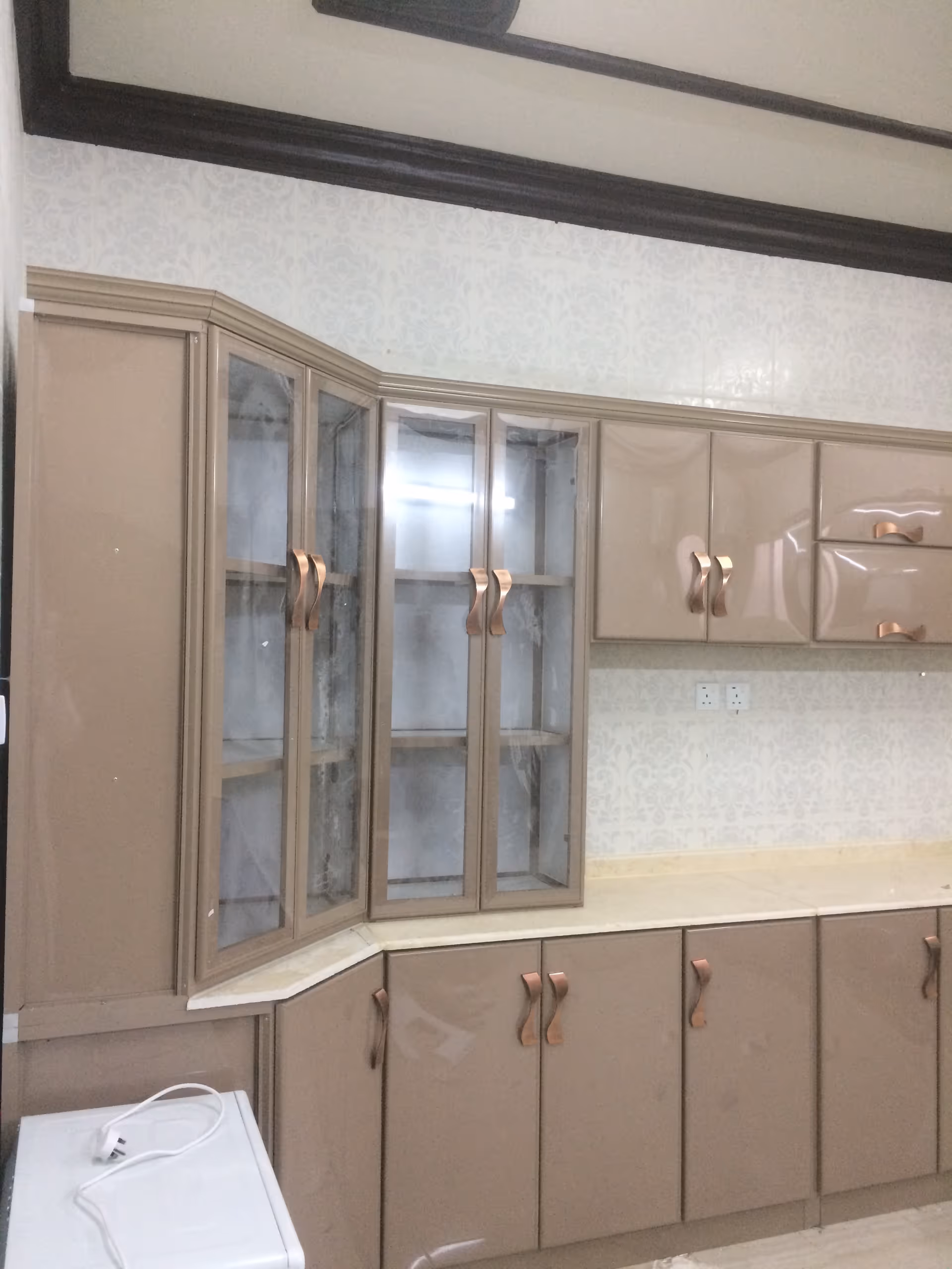 Beige kitchen cabinets and glass-front pantry along a wallpapered wall.