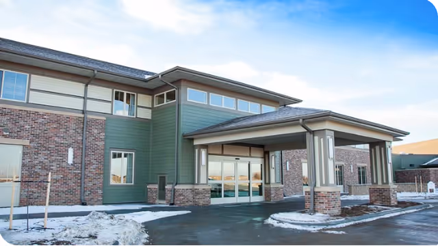 Exterior view of Fallbrook Assisted Living and Memory Care entrance with brick and green siding.