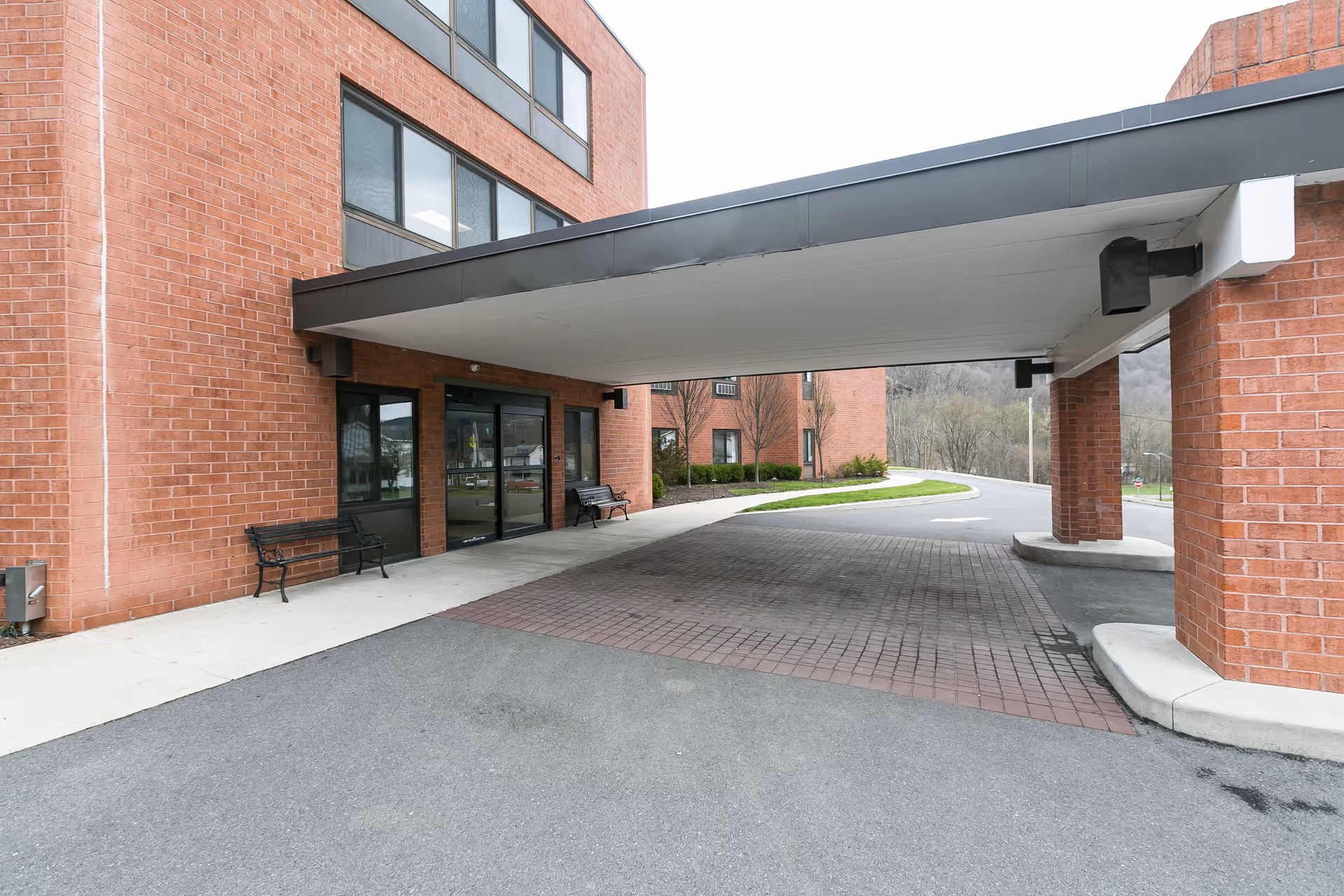 Covered porte-cochere entrance of a brick building with benches and sliding glass doors.