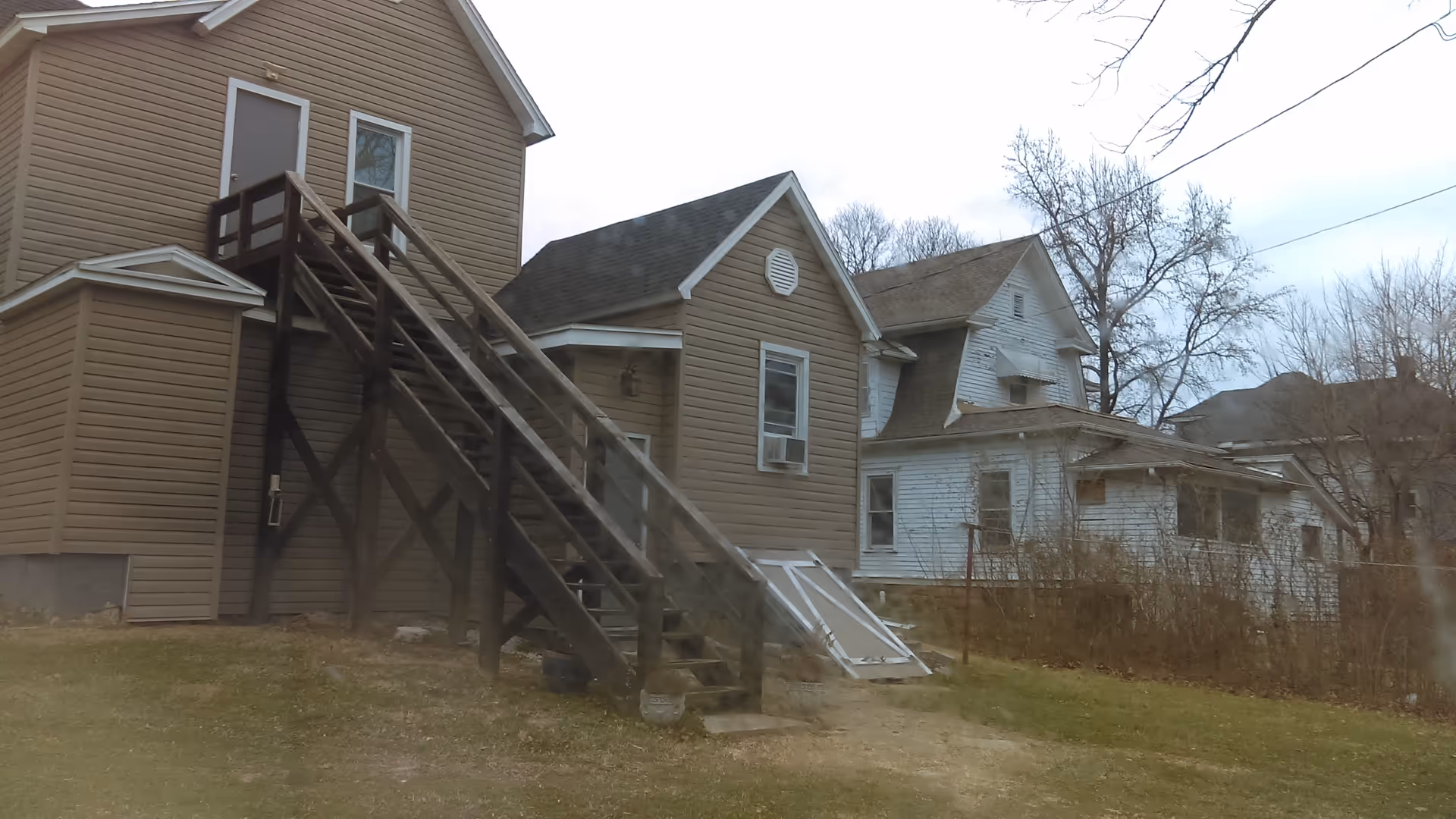 Two houses with wooden stairs and a metal ramp in a yard.