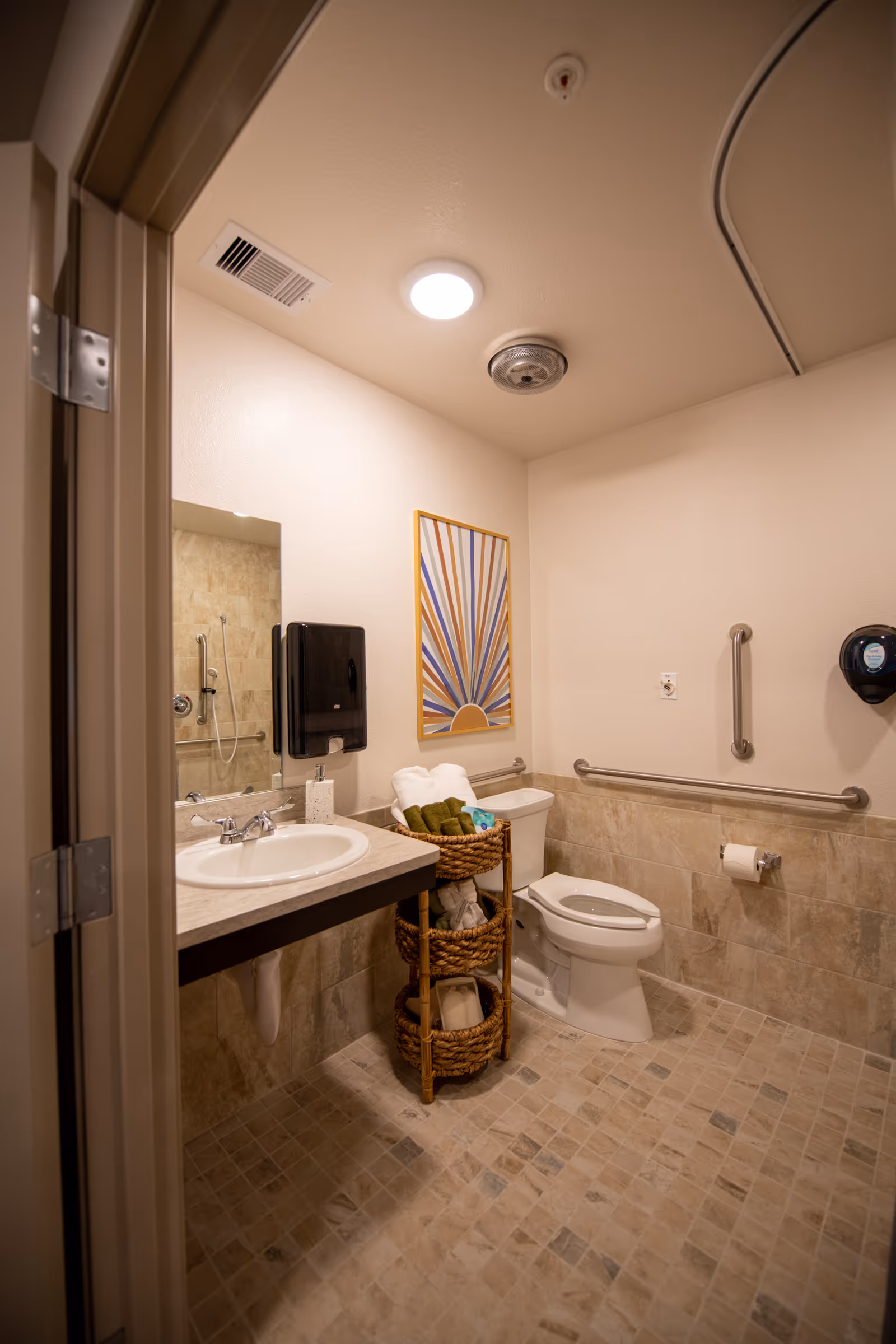 Accessible bathroom with sink, toilet, grab bars, and towels in a senior living facility.