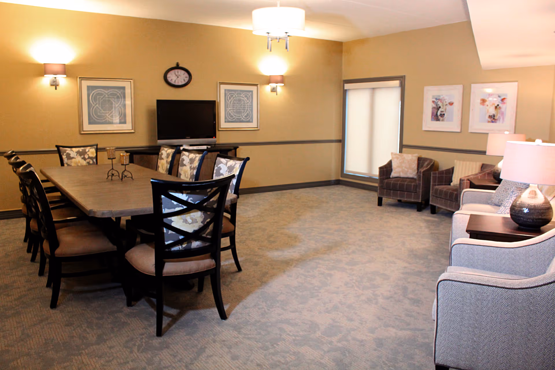 A spacious senior living common area with a large dining table and lounge seating.