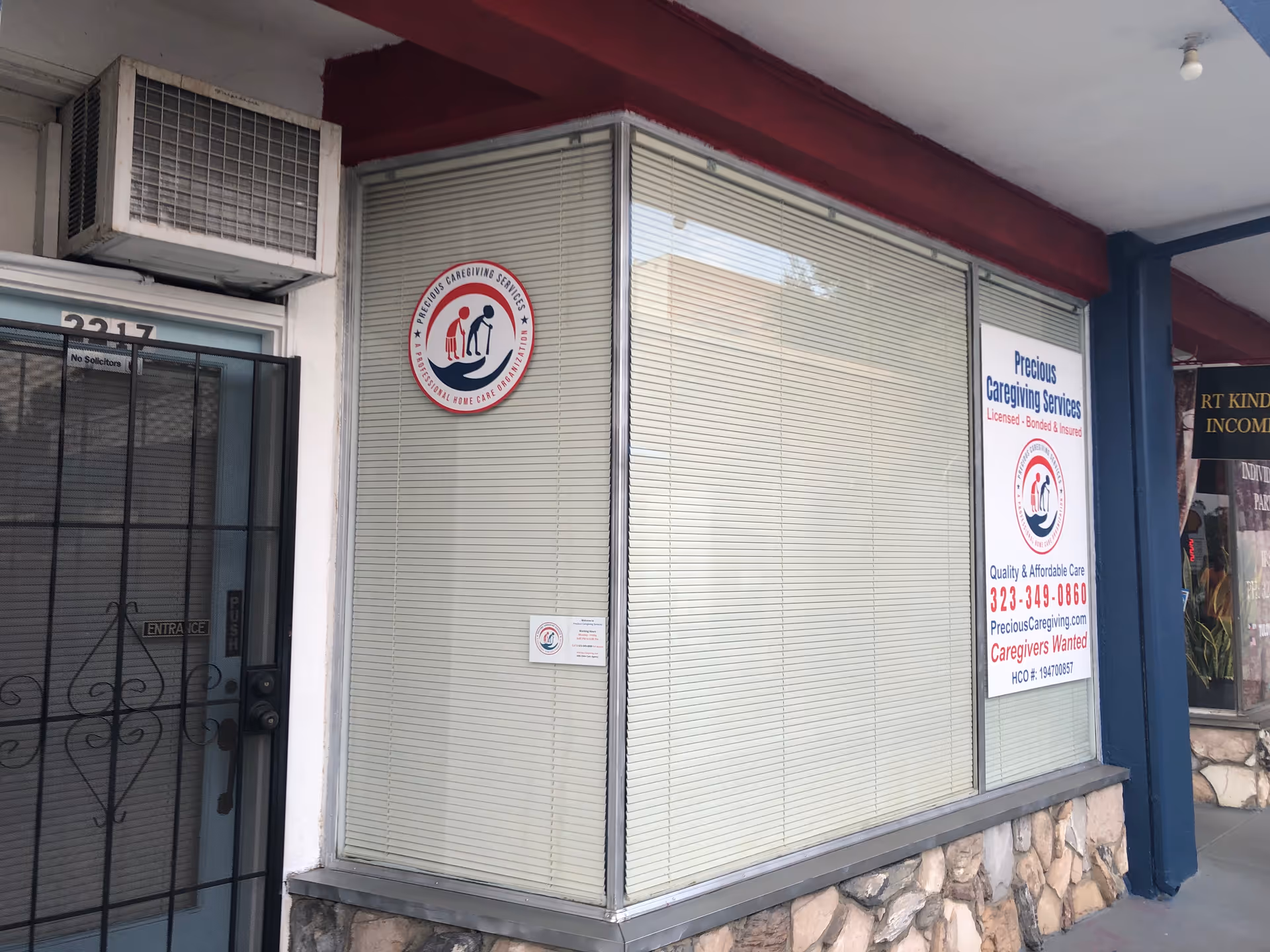 Storefront with large windows, beige blinds, and a Precious Caregiving Services sign.