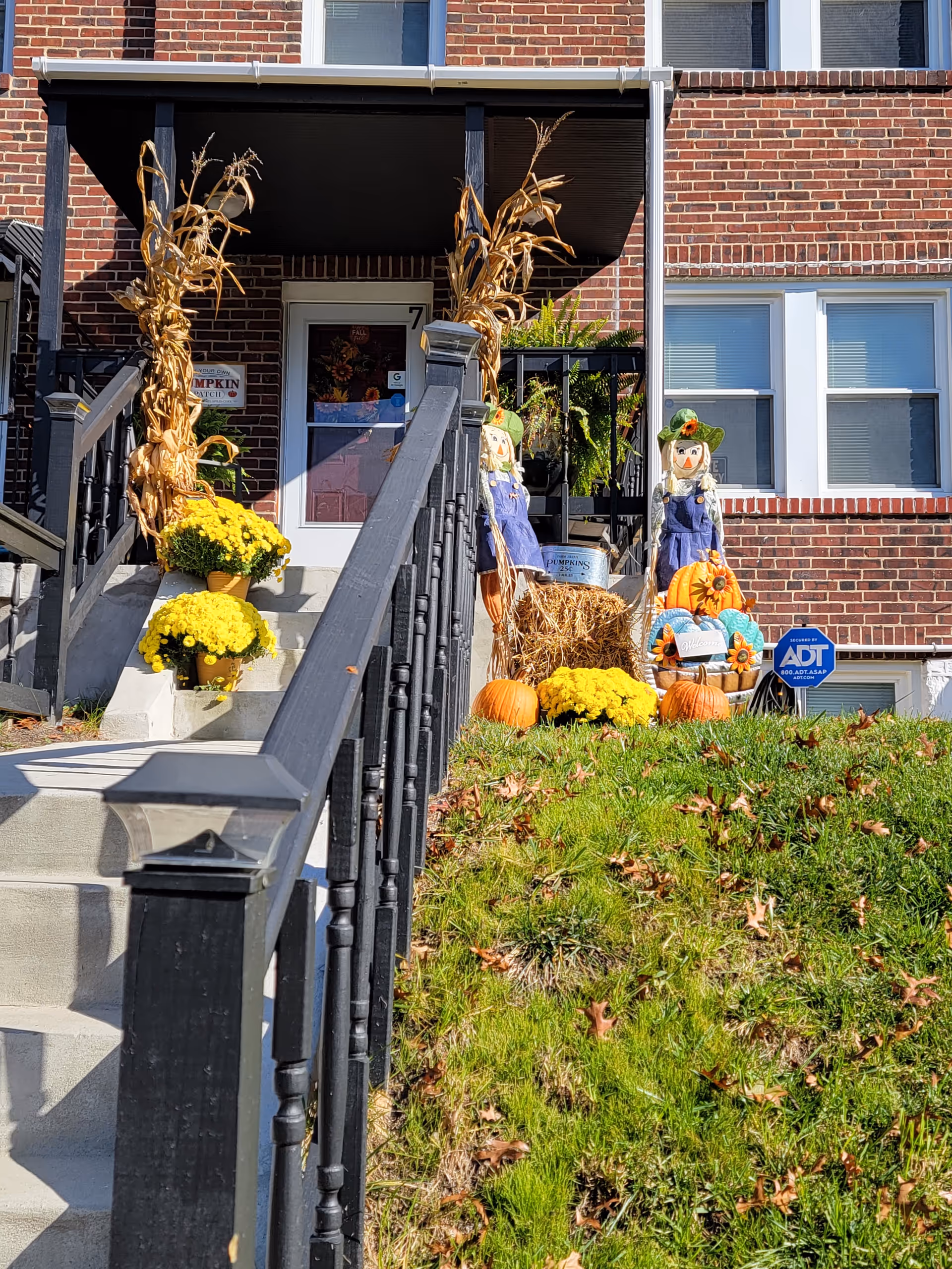 Brick building entrance decorated with pumpkins, cornstalks, and mums on steps.