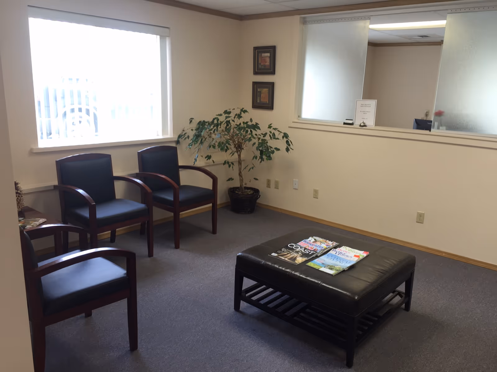 Waiting area with four chairs, a potted plant, and a magazine-covered ottoman.