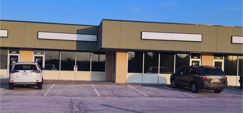 Front view of a single-story commercial building with large windows and parked cars.