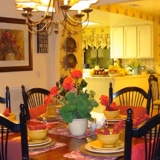 A cozy dining room with a round table, chairs, and a bright kitchen in the background.