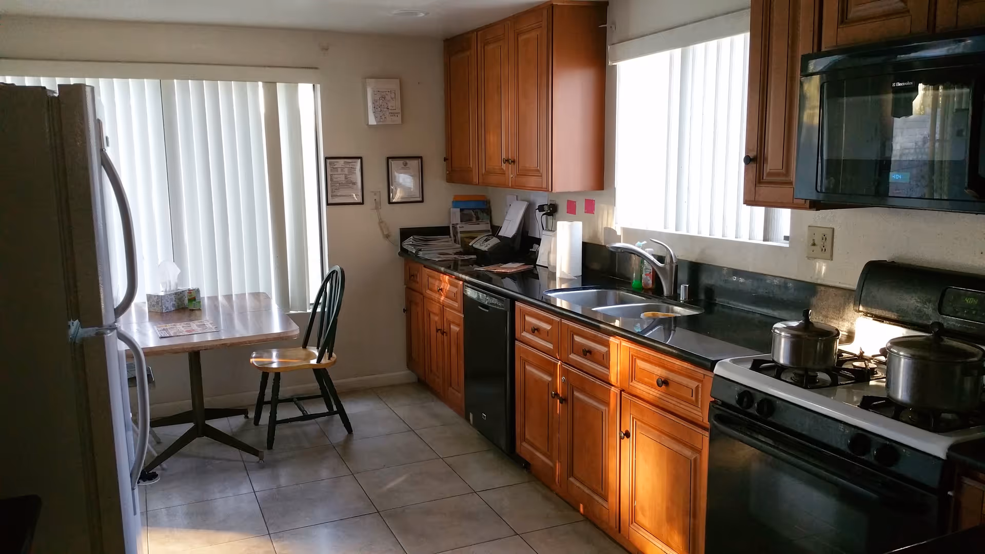Kitchen with wooden cabinets, black countertops, stainless sink, stove, and a small table.