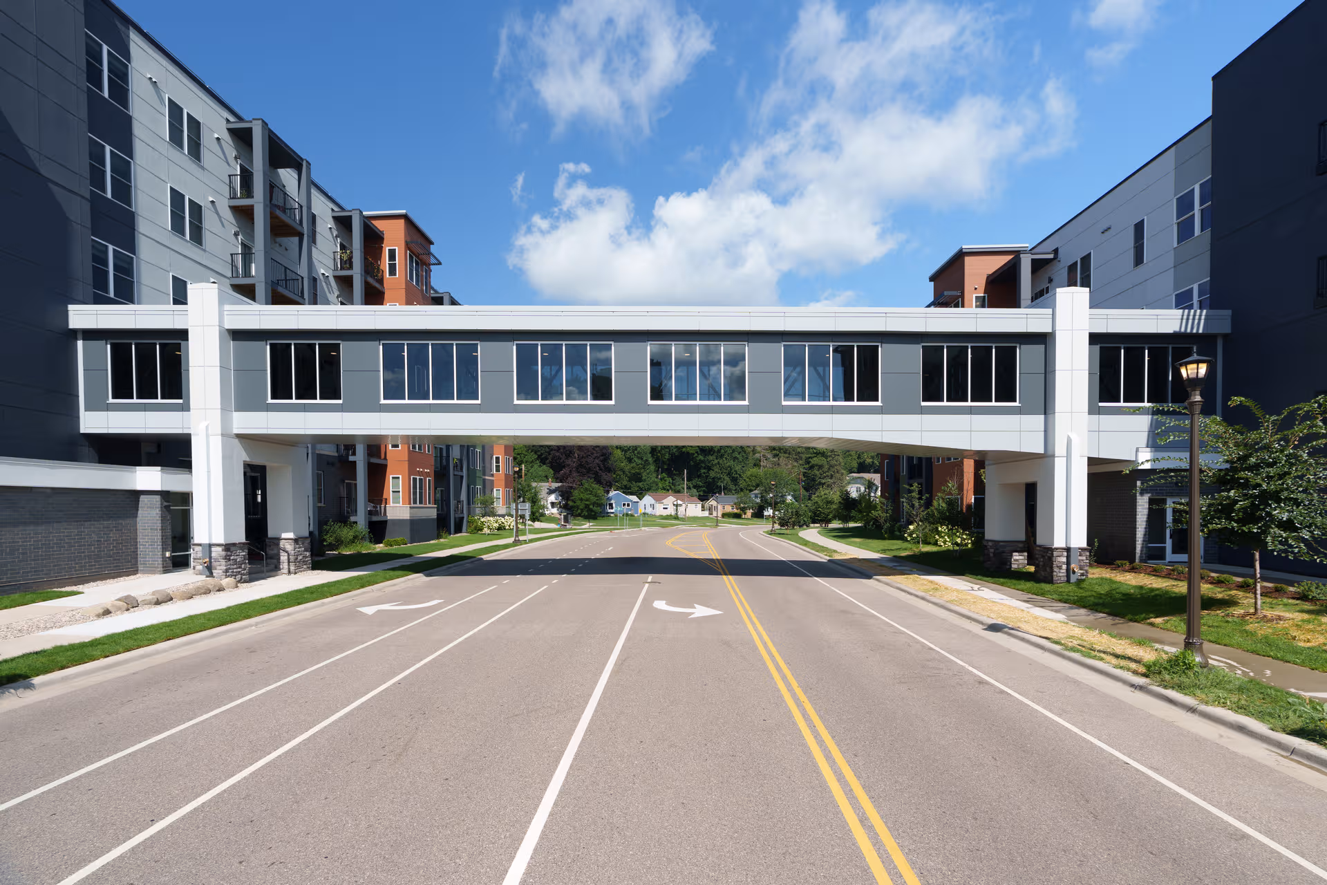 Modern Lexington Landing senior living building with a skybridge over a street and blue skies.
