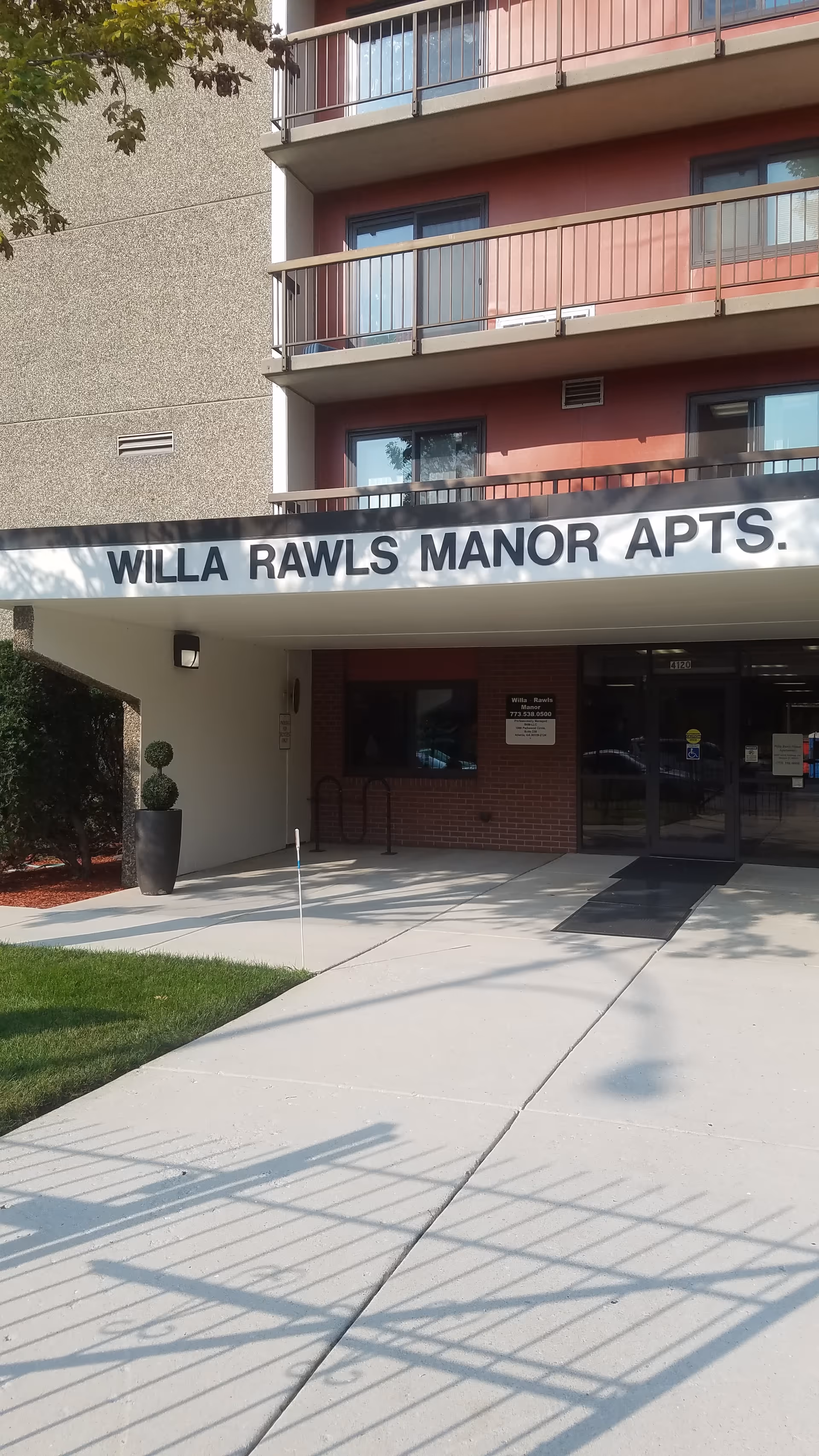 Facade of Willa Rawls Manor Apartments with balconies and glass entrance doors.