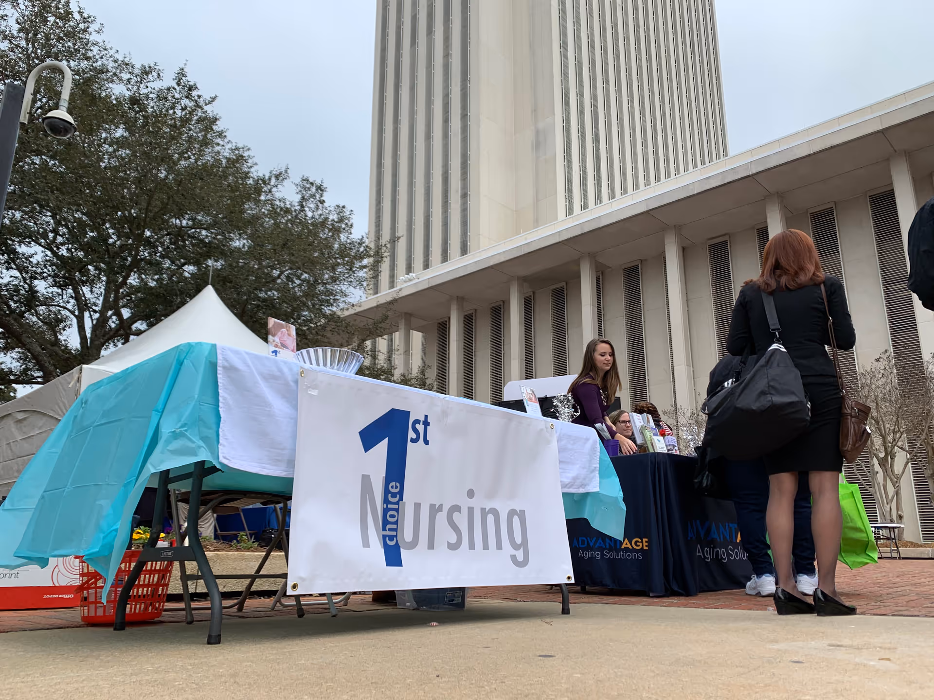 Outdoor nursing expo booth with 1st Nursing banner in front of a tall campus building.