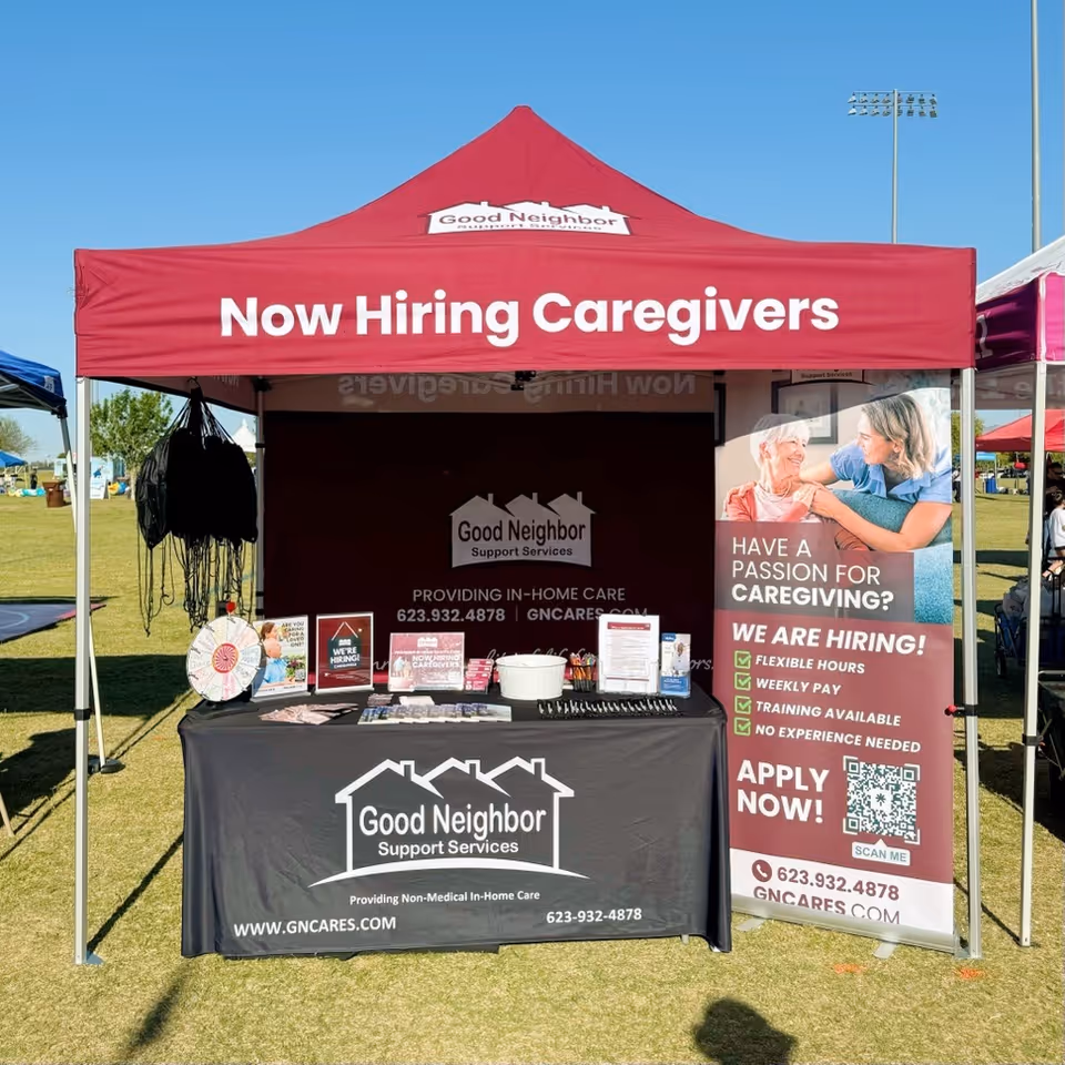 Outdoor booth promoting Good Neighbor Support Services with a 'Now Hiring Caregivers' banner.