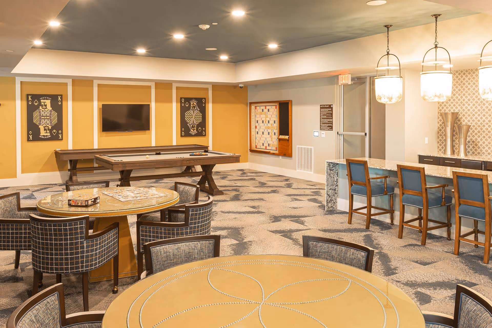 Community game and lounge room with card tables, a pool table, a wall-mounted TV, and a bar counter with pendant lights.