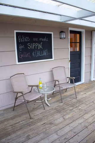 Two patio chairs and a small table sit on a wooden deck beside a chalkboard sign.