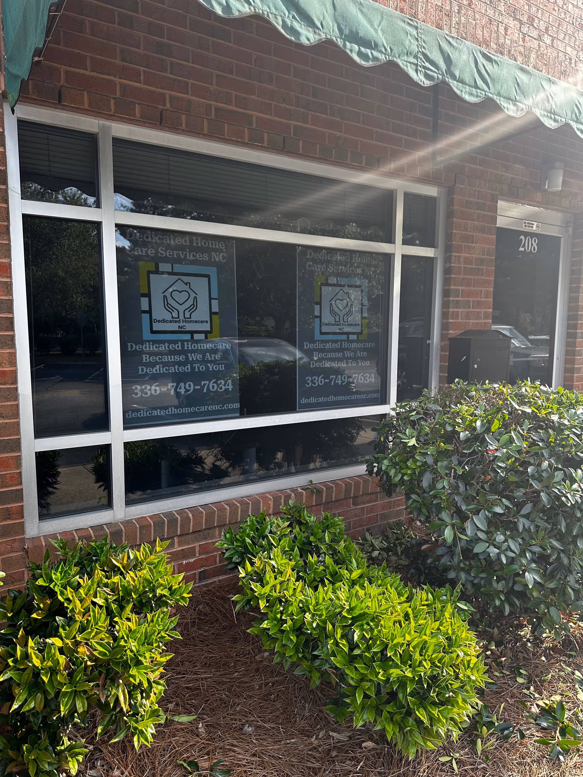 Brick building storefront with large windows, dedicated homecare signs, and trimmed bushes.