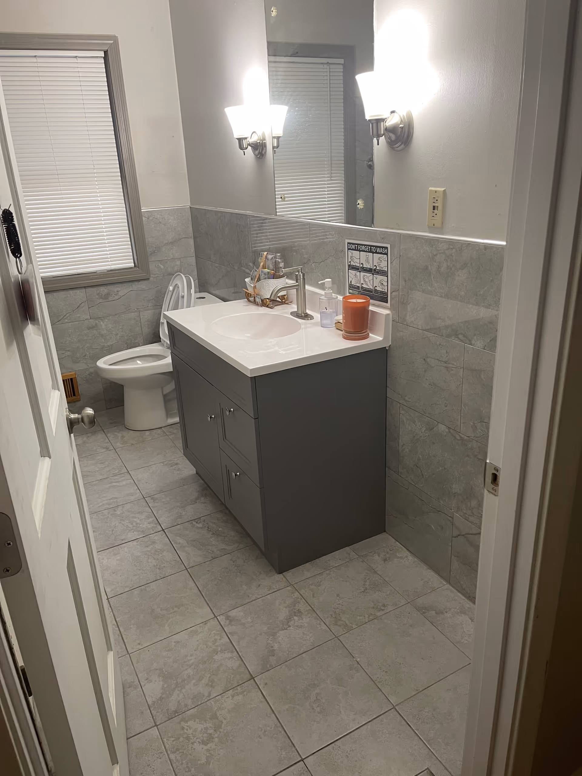 Gray bathroom with sink vanity, mirror, toilet, and tiled walls in a senior living facility.