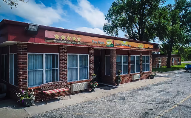 Brick, single-story building with windows, banner, bench, and planters outside a parking area.