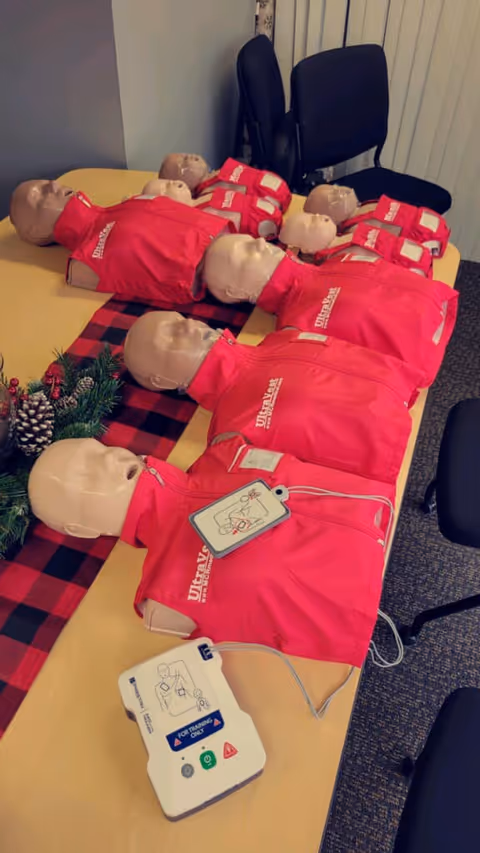 Row of CPR training mannequins in red vests on a long table.