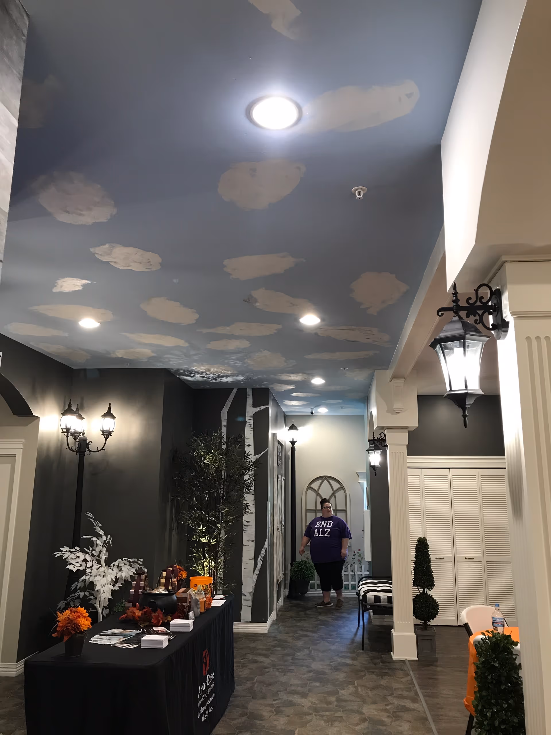 Indoor hallway with cloudy ceiling, decorative lamps, and a person wearing a purple END ALZ shirt.