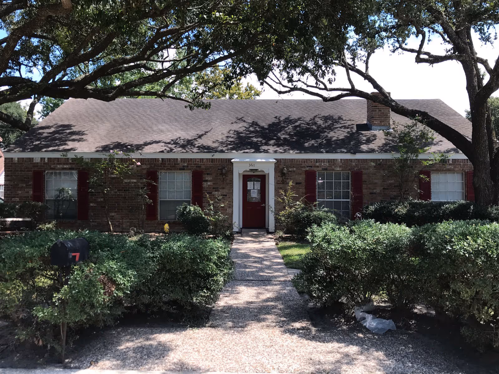 Brick single-story cottage-style building with a red door, white trim, front walkway, and shrubs.