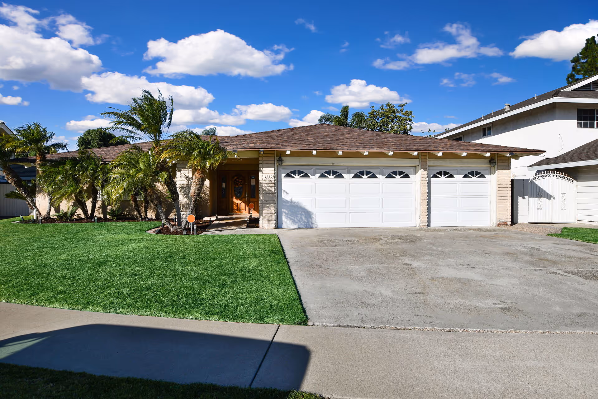 Front view of a care home: single-story, three-car garage, palm trees, blue sky.